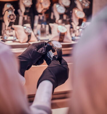 Shop assistant in black gloves is showing expensive watch for a customer
